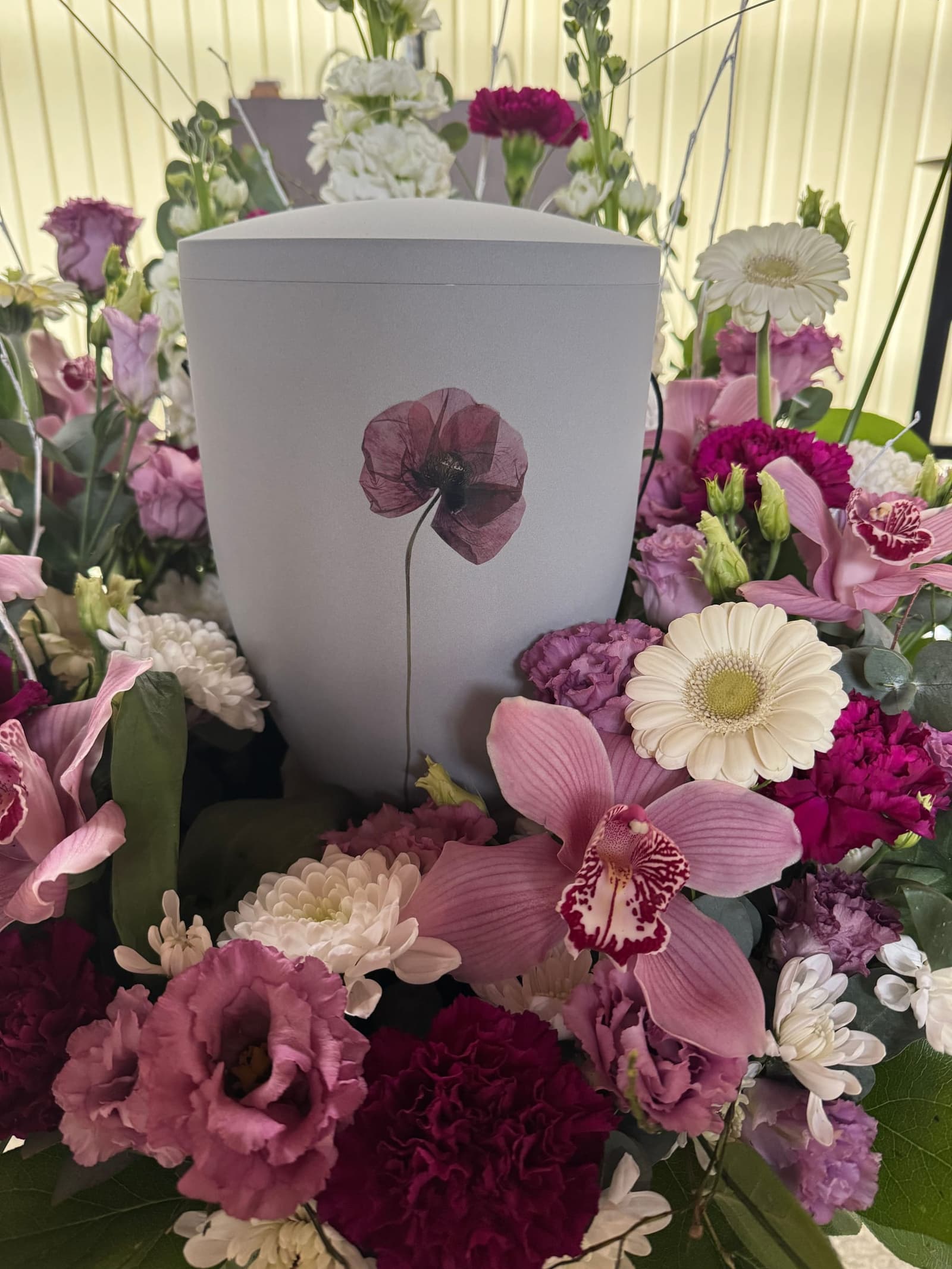 Weiße Urne mit gemalter Mohnblume, umgeben von Orchideen, Nelken und Margeriten
